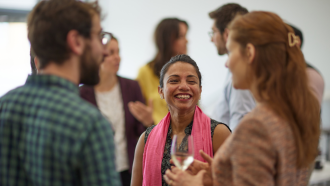 Mahreen Khan standing in a group smiling and wearing a pink scarf.