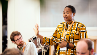 Anne Makena wearing an orange patterned dress presenting to a crowd at the Skoll Community Convening.