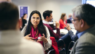Sugandha Srivastav wearing a pink scarf and talking to other conference attendees.