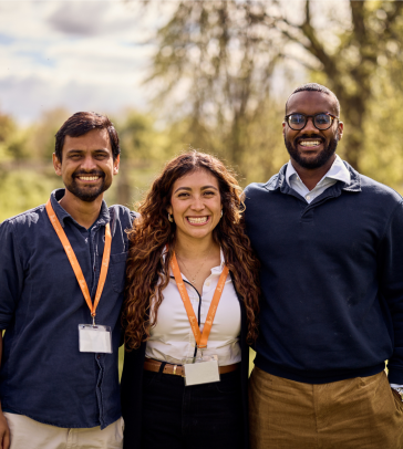 Saransh standing and smiling in a green meadow with the other 2025-26 Skoll Scholars, Luisa and Yousif.