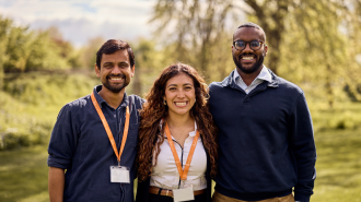 Saransh standing and smiling in a green meadow with the other 2025-26 Skoll Scholars, Luisa and Yousif.