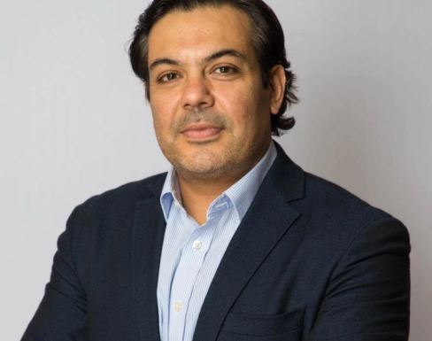Abrar crossing his arms and smiling wearing a blue suit. 