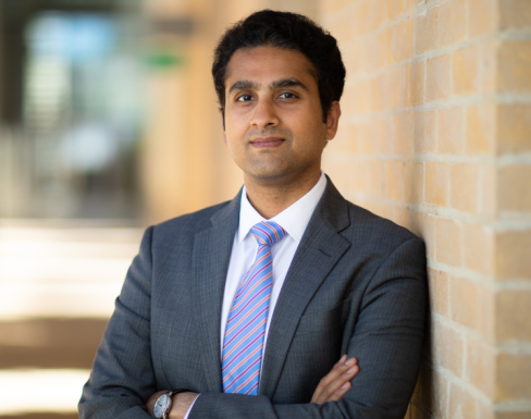 Akshay Mangla standing in the SBS hallway wearing a grey suit and smiling. 