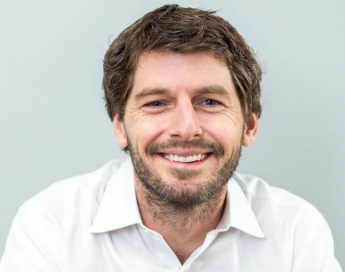 Hudson Baird in front of a light background smiling wearing a white shirt.