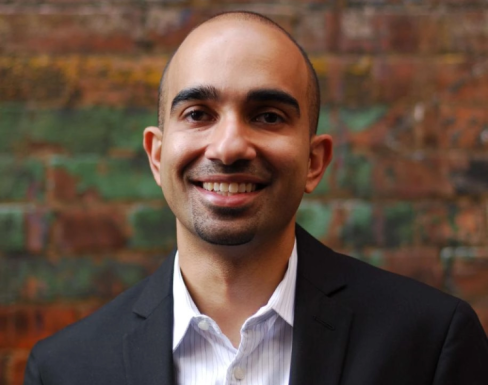 Karim Harji standing in front of a brick wall wearing a suit and smiling. 