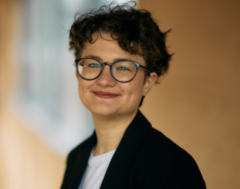 Elizaveta Belkina standing in the SBS hallway smiling wearing a suit. 