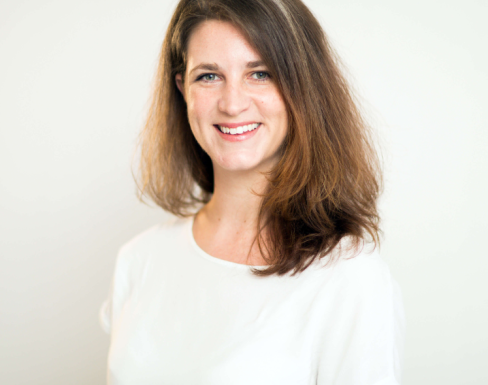 Pip Wheaton standing in front of a light background wearing a white top and smiling.