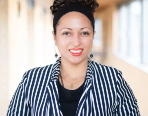 Tara Sabre Collier stood in an SBS hallway, smiling, and wearing a striped jacket. 