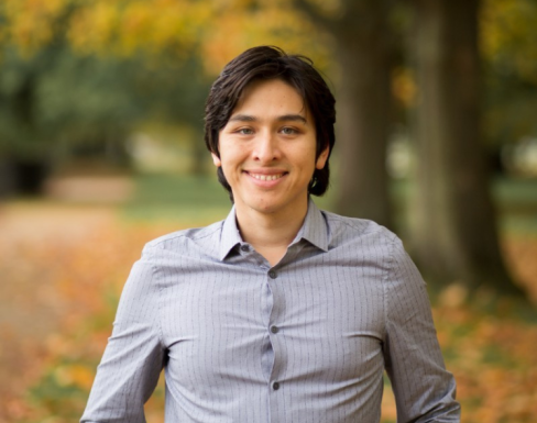 Alexander Wankel smiling in front of a leafy background. 