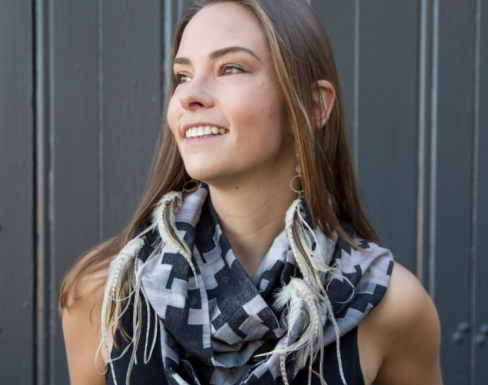 Anima La Voy wearing a grey scarf in front of an industrial building smiling. 