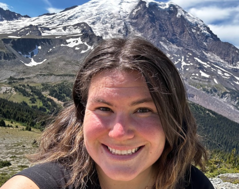 Ashley Thomas smiling in front of a scenic mountain landscape.