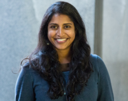 Christie George smiling in front of a grey background wearing a blue sweater.