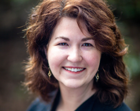 Claire Wathen smiling in front of a natural blurred background, wearing a navy blouse.