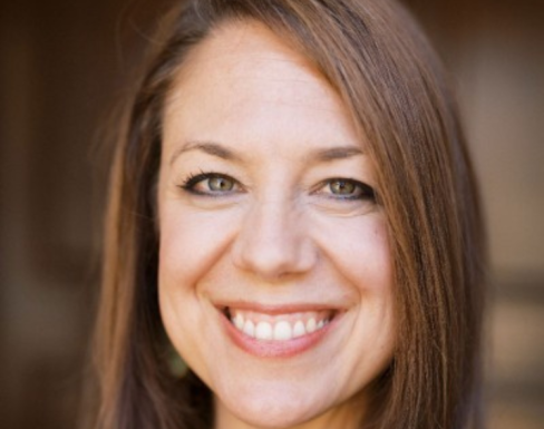 Cynthia Rayner smiling in front of a brown background.