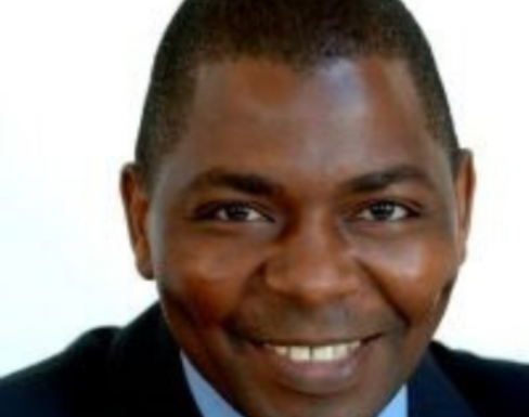 David Muhia sitting in front of a white background in a suit and tie.