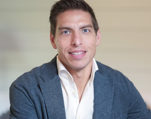 Derrick Feldmann wearing a pale shirt and grey blazer, smiling. 