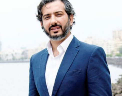 Dhruv Lakra standing in front of the sea in a pink shirt and blue blazer.