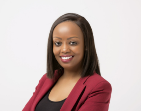 Diana Wangari is smiling in a crimson blazer and black top with her arms crossed, in front of a white background.