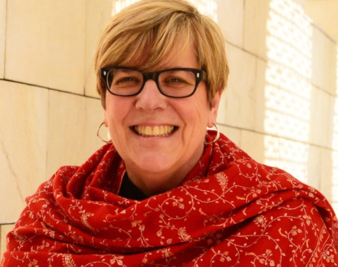 Gayle Peterson smiling in the Said Business School courtyard in the sun, wearing a red shawl.