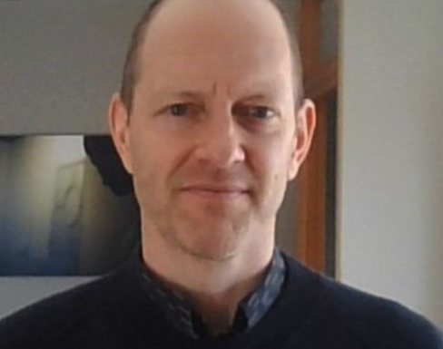 Jesse Fahnestock standing in front of a beige wall wearing a dark grey sweater.