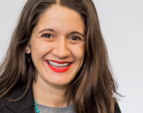 Jessica Shortall smiling in front of a grey background wearing a black blazer.