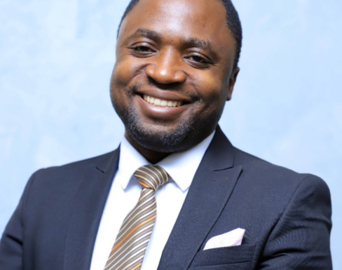 John Kakungulu Walugembe wearing a suit in front of a blue background.