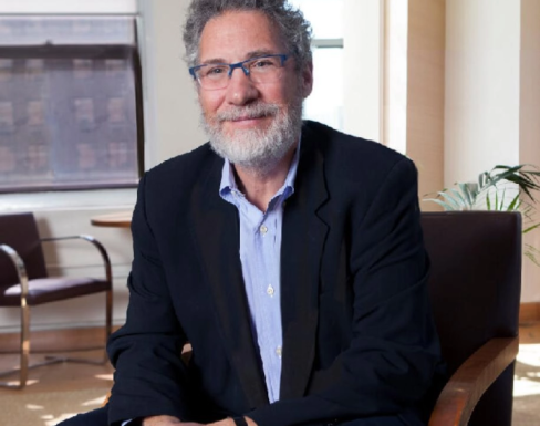 Jonathan Rose smiling, sat in the corner of a bright office wearing a dark navy suit and blue shirt.