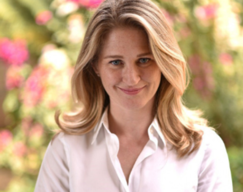 Jordyan Corcoran standing in front of a flowery background wearing a white shirt and smiling. 