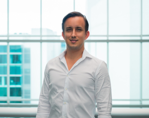 José Miguel Alfaro Gómez standing in a glass hallway wearing a shirt and smiling. 