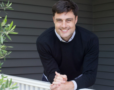 Louis Dorval leaning over a gate and smiling. 