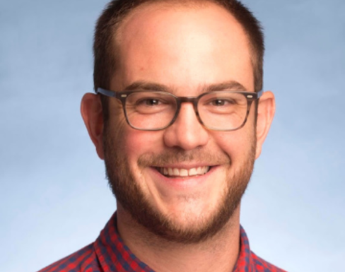 Mark Clayton Hand wearing a plaid red shirt and smiling. 
