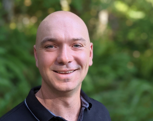 Nigel Tunnacliff standing in front of a leafy background smiling. 