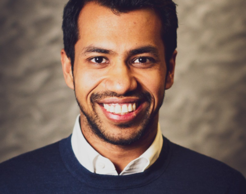 Ritesh Singhania wearing a jumper and shirt and smiling. 