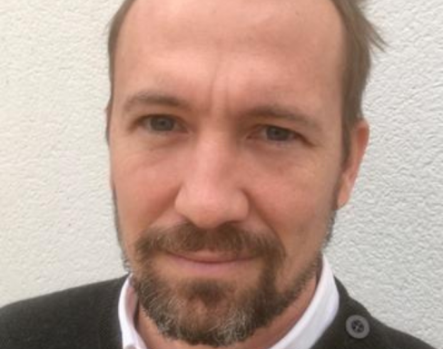 Rob Pettit standing against a white wall wearing a black jumper.