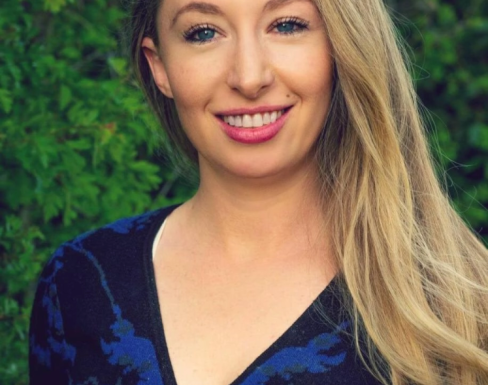 Sophie Maclaren smiling in front of a green hedge wearing a blue top.
