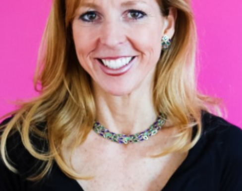 Tara Roth McConaghy smiling in front a bight pink background wearing a black top.