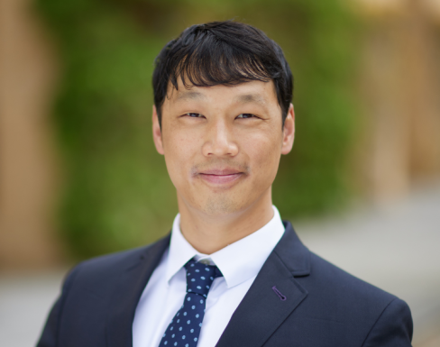 Kevin Tang standing in the SBS hallway wearing a navy suit and smiling. 