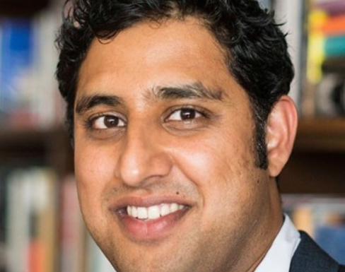 Rajiv Joshi smiling in front of a bookcase.