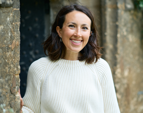 Jessica Jacobson standing in a college doorway wearing a white jumper and smiling. 