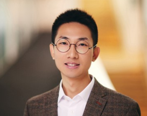 Cheng Li standing in the SBS hallway wearing a brown suit.