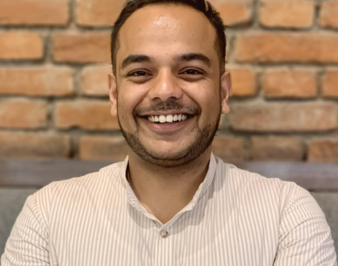 Achyut Gautam standing and smiling in front of a brick wall. 