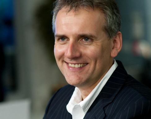 Sean Hinton smiling off to the side, wearing a dark navy suit. 