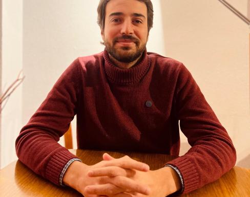 Sebastián Jaramillo wearing a red jumper crossing his arms and smiling at a desk. 