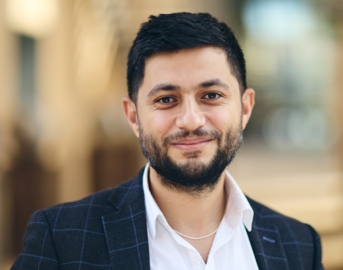 Closeup shot of Ammar in a white shirt and navy blazer, smiling at the camera