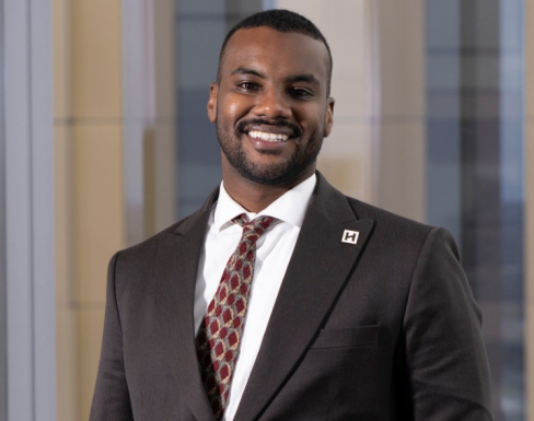 Yousif Yahya is smiling and wearing a suit in front of a building window. 