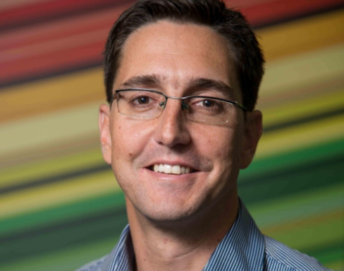 Francois is smiling in front a multicoloured background, smiling and wearing a light blue shirt. 