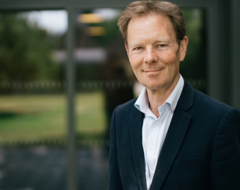 Jonathon is wearing a dark suit and smiling in front of a bright window. 