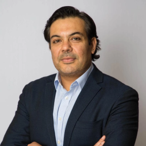 Abrar crossing his arms and smiling wearing a blue suit. 