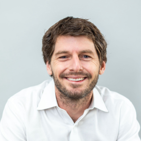 Hudson Baird in front of a light background smiling wearing a white shirt.