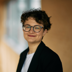 Elizaveta Belkina standing in the SBS hallway smiling wearing a suit. 